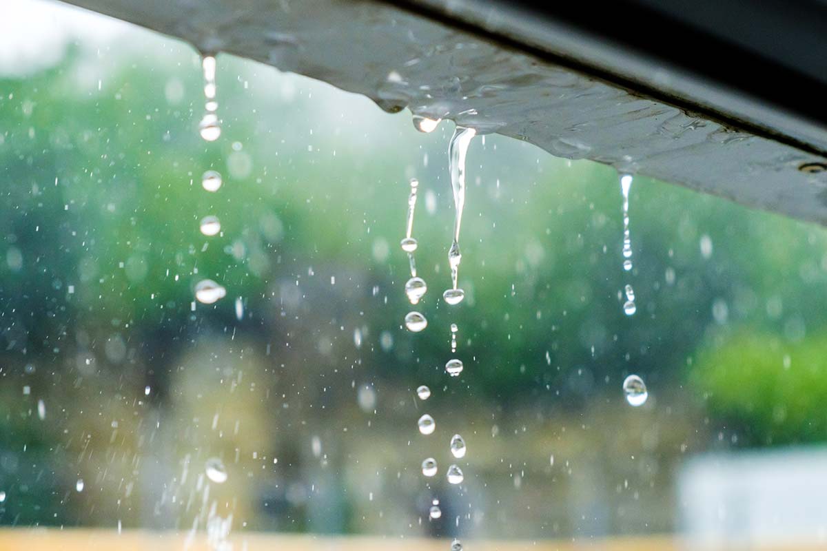 Close-up of overflowing gutters with clear rainwater droplets falling during a heavy rainstorm.