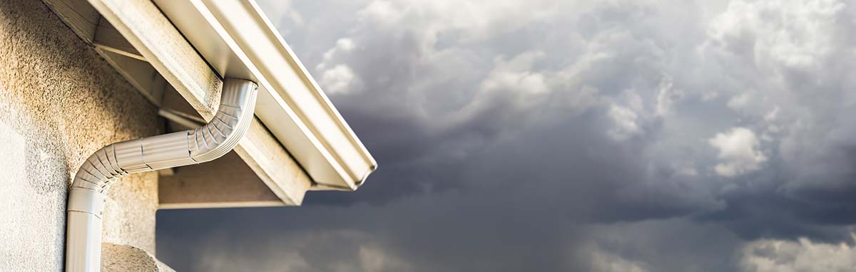 Gutters on a house against a stormy sky, potential for overflowing due to impending heavy rainfall.