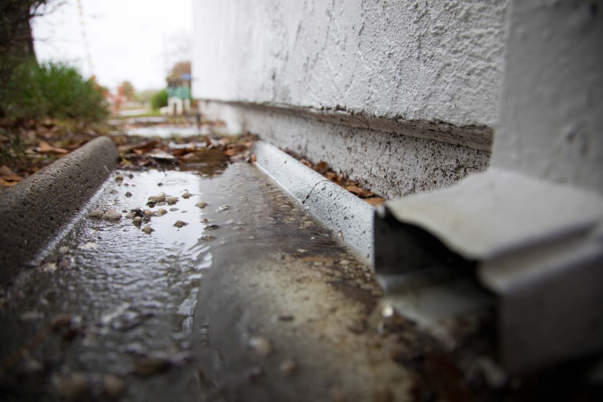 Puddle of water on a concrete surface next to a building, indicative of recently overflowed gutters.