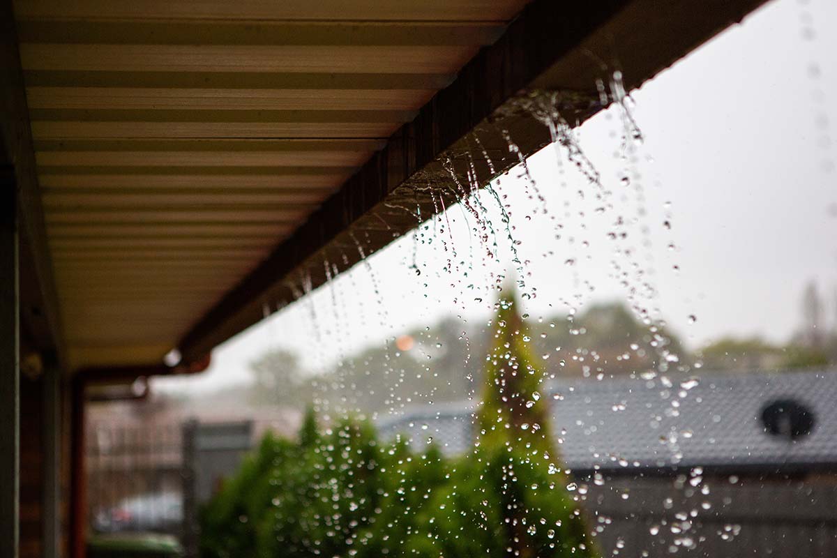 Heavy rain overflowing a gutter during a storm, illustrating How Rain Gutters Protect Arizona Homes During Monsoon Season
